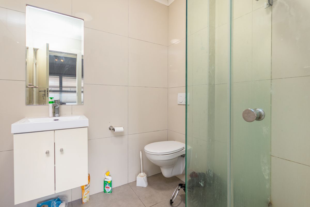 Modern bathroom featuring a wall-mounted toilet, vanity basin with mirror, and a glass-enclosed shower with neutral floor-to-ceiling tiling.