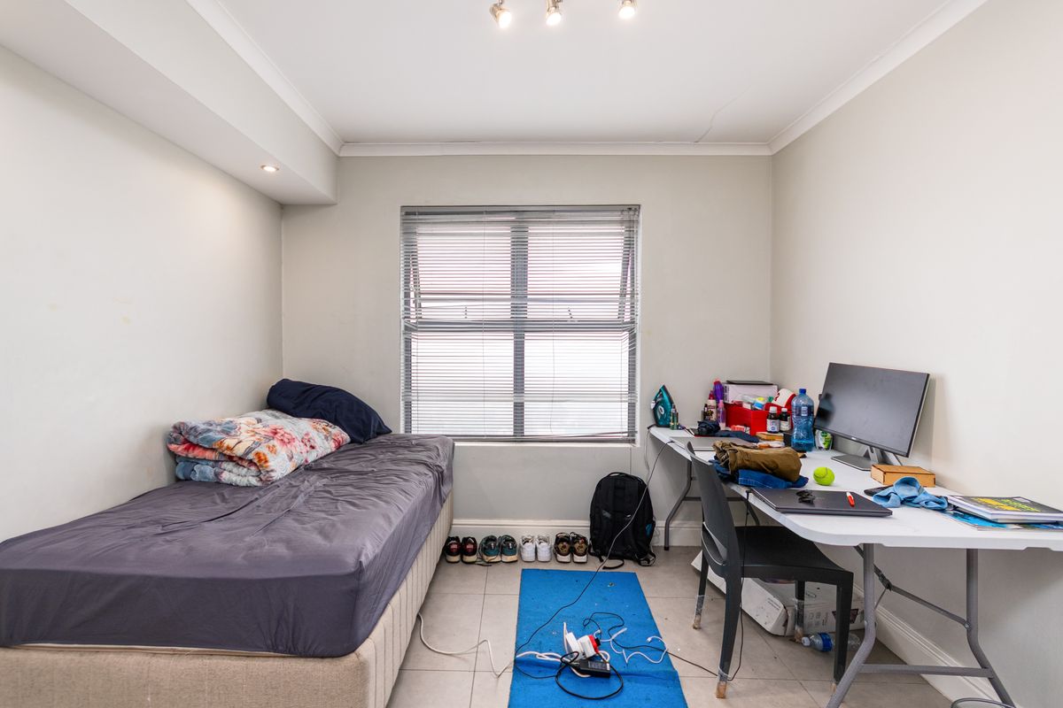 A functional bedroom featuring tiled flooring, a central window with fitted blinds, and recessed ceiling lighting.