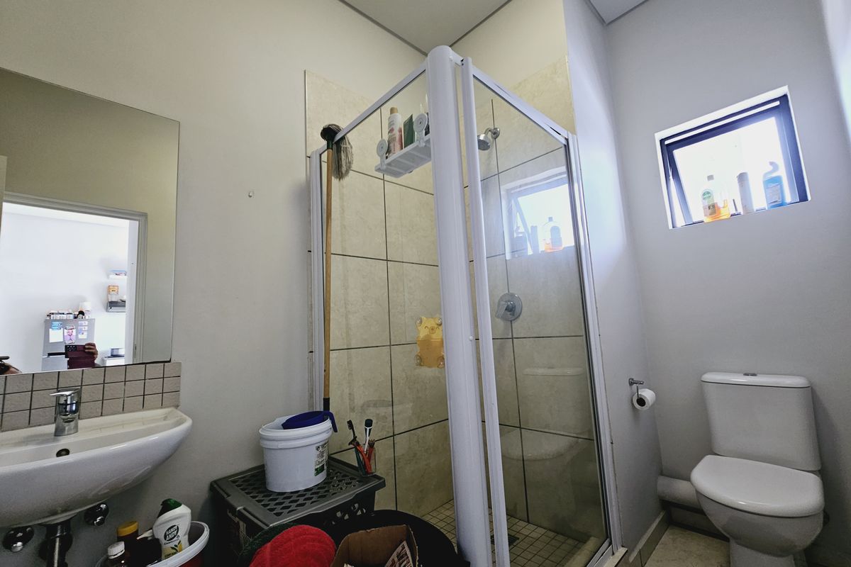 A functional bathroom featuring a glass-enclosed shower, pedestal basin, and standard toilet with tiled flooring and neutral wall finishes.