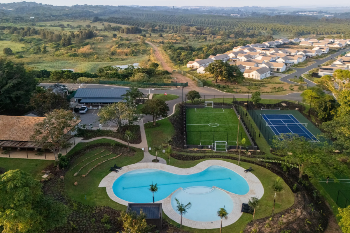 Aerial view of a residential estate featuring a swimming pool, soccer field, tennis court, and clubhouse surrounded by landscaped grounds.