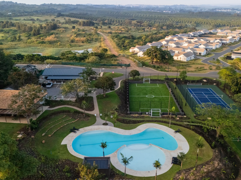 Aerial view of a residential estate featuring a swimming pool, soccer field, tennis court, and clubhouse surrounded by landscaped grounds.