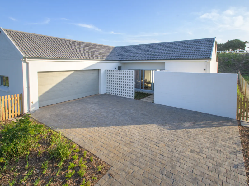 Modern residential facade featuring a paved driveway, automated garage, and decorative breeze block screen, set within a well-maintained landscaped environment.
