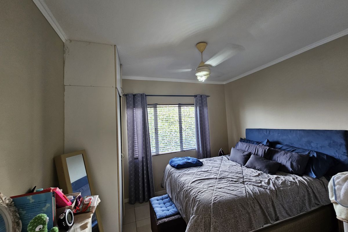 A functional bedroom featuring built-in cupboards, a ceiling fan, and tiled flooring, offering a comfortable and practical living space.