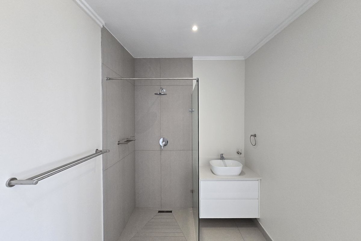 Modern bathroom featuring a walk-in shower with glass screen, wall-mounted vanity with vessel sink, and neutral floor-to-ceiling tiling.