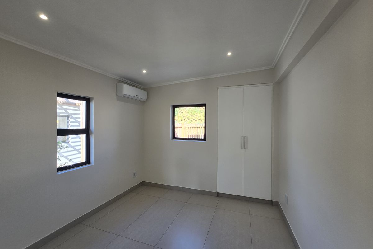 A clean, modern bedroom featuring neutral tiled flooring, built-in wardrobe storage, and an integrated air conditioning unit.