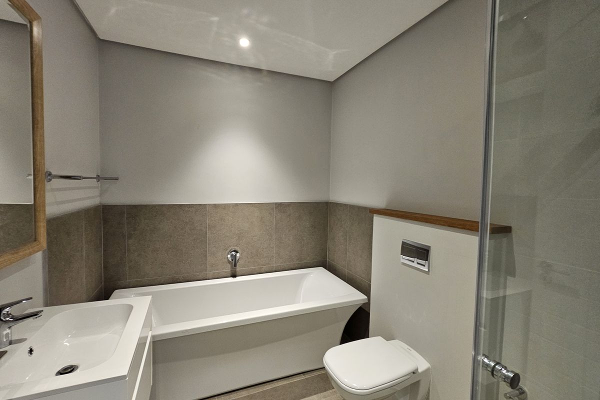 Modern bathroom featuring a sleek freestanding bathtub, wall-mounted toilet, vanity basin, and a glass-enclosed shower with contemporary neutral tiling.