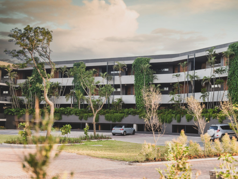 Modern multi-level apartment complex featuring contemporary architectural design, integrated vertical gardens, and landscaped grounds with paved driveway access.