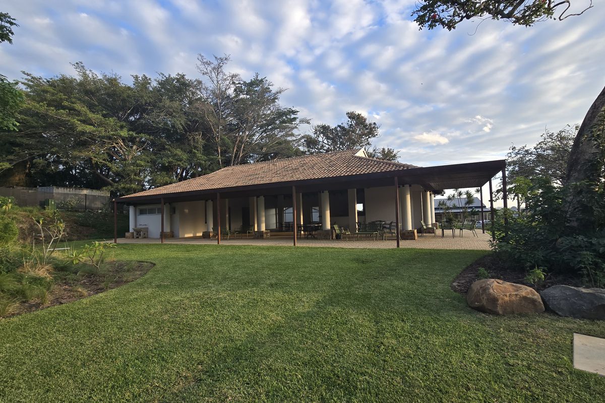 A spacious rear exterior view featuring a large covered patio with tiled roofing, support columns, and a well-maintained lawn and garden area.