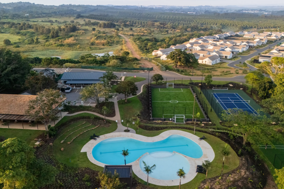 Aerial view of a residential estate featuring a swimming pool, tennis court, soccer field, and clubhouse surrounded by landscaped grounds.