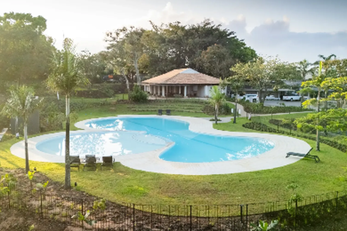 An elevated view of a well-maintained swimming pool set within a landscaped garden area, featuring paved surrounds and perimeter fencing.