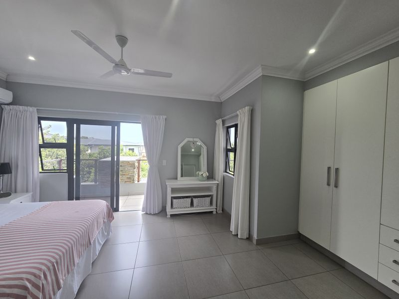 Spacious bedroom featuring neutral tiled flooring, built-in cupboards, recessed lighting, a ceiling fan, and sliding glass doors leading to an outdoor balcony.