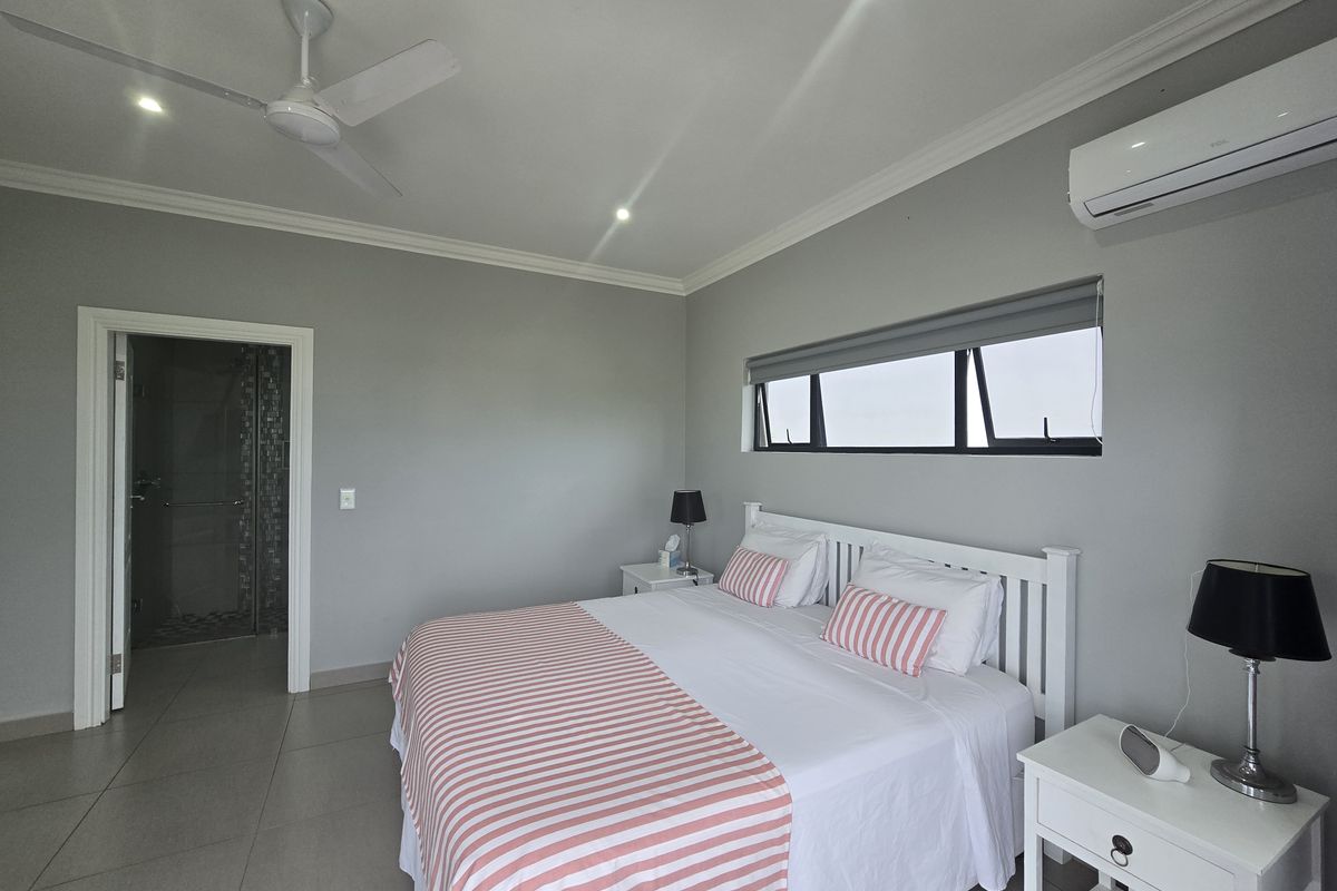 A well-maintained bedroom featuring tiled flooring, a ceiling fan, split-system air conditioning, and direct access to an en-suite bathroom.