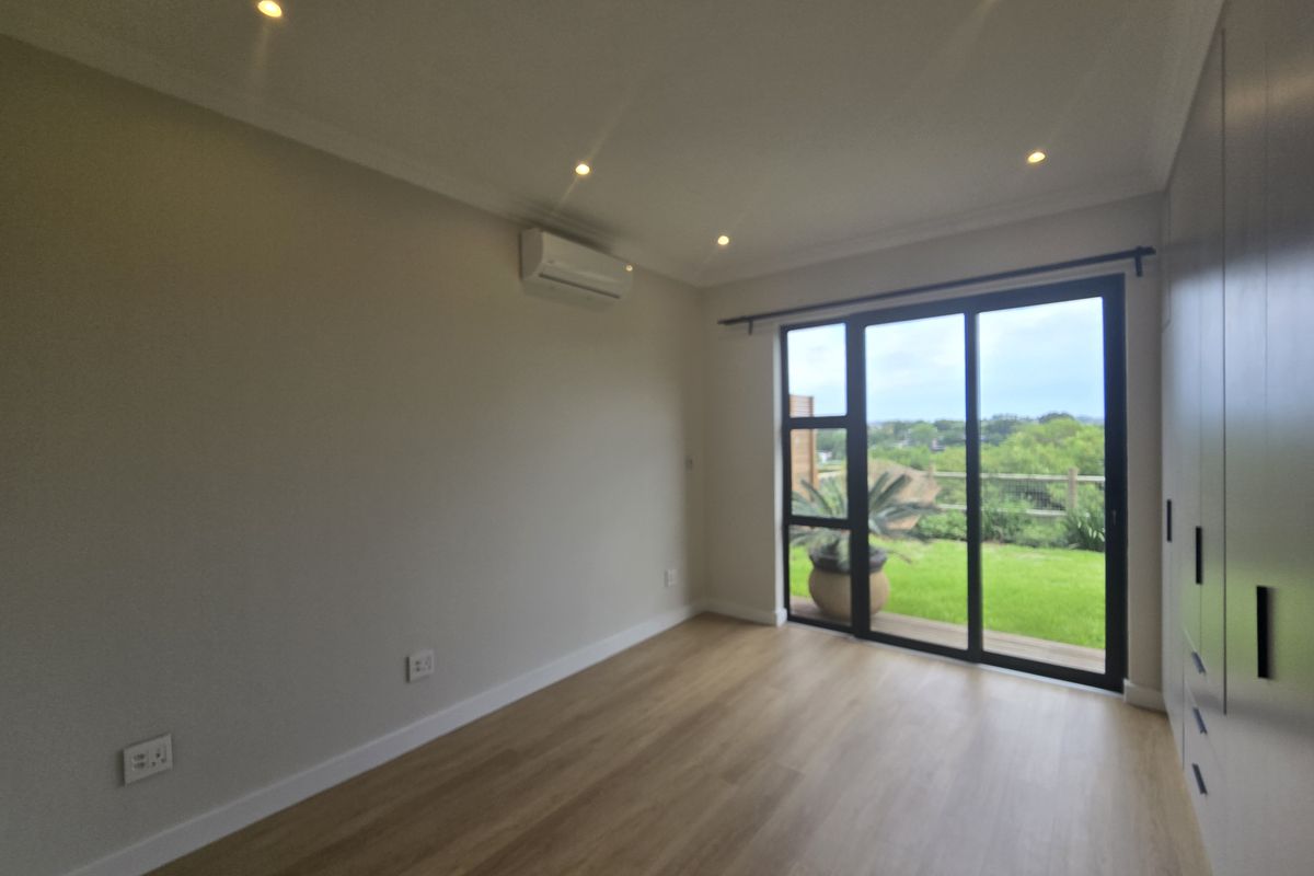 A bright, modern bedroom featuring laminate flooring, built-in wardrobes, recessed lighting, and a sliding glass door providing access to the garden.