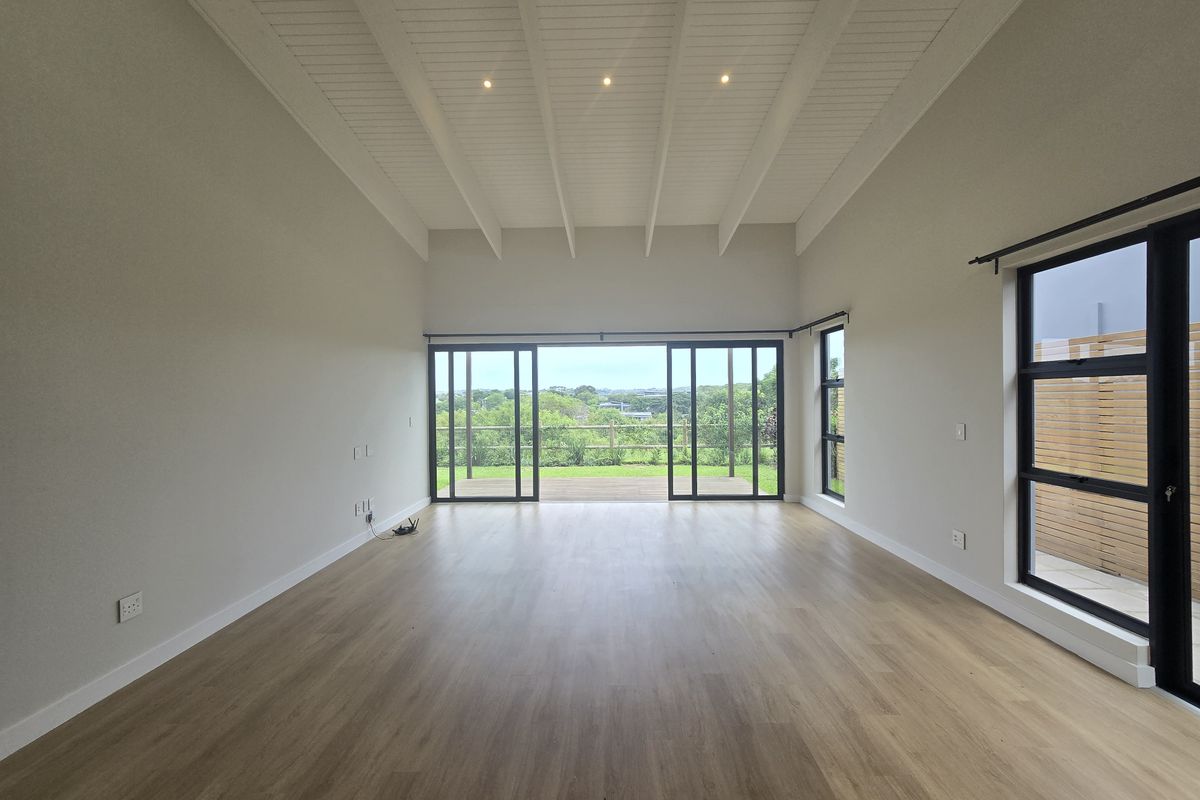 Spacious, light-filled living area featuring vaulted ceilings with exposed beams, modern laminate flooring, and large sliding glass doors opening to an outdoor deck.
