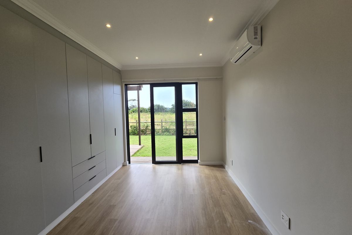 A bright, modern bedroom featuring extensive built-in cabinetry, laminate flooring, recessed lighting, and direct access to a private garden through a sliding glass door.