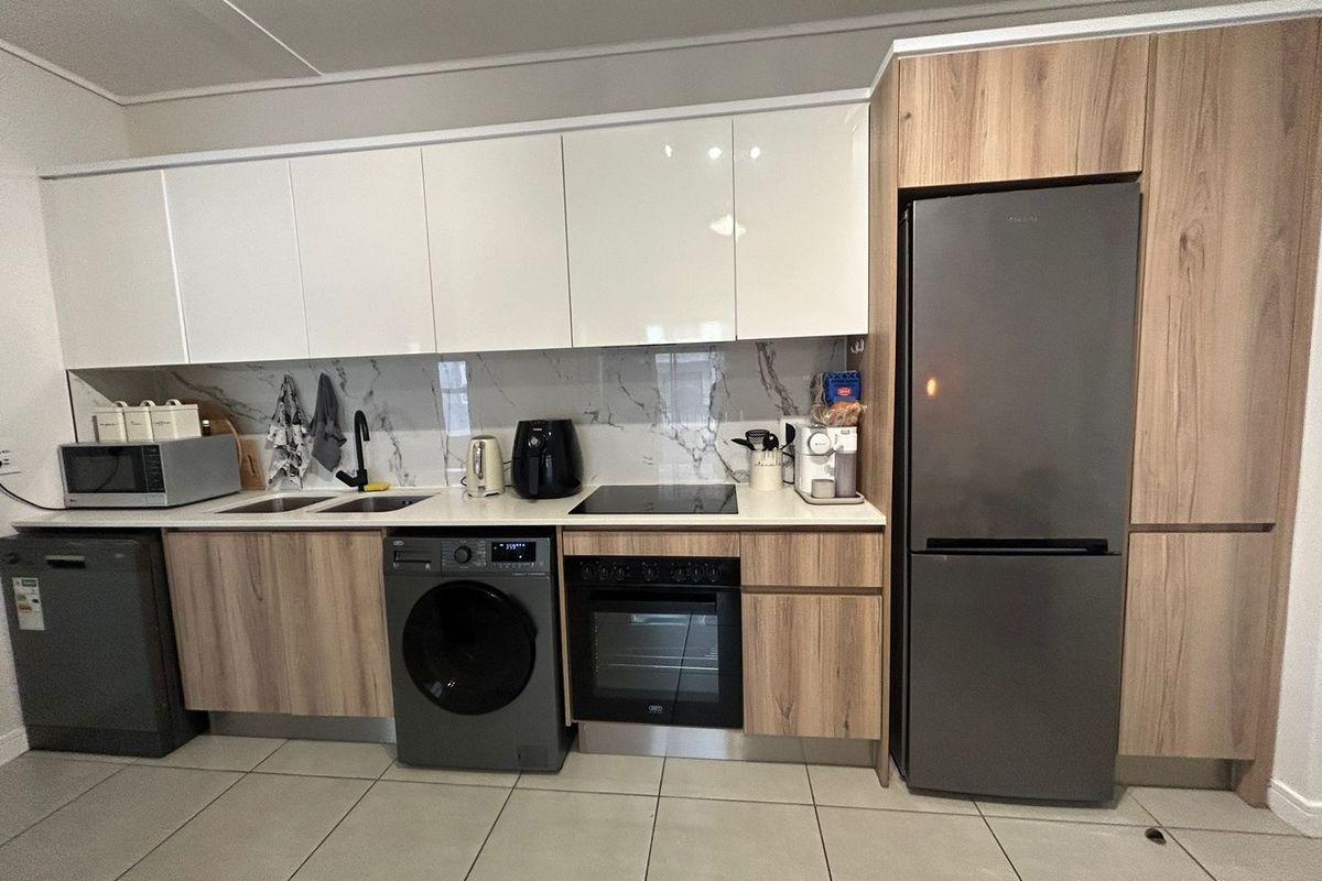Modern kitchen featuring sleek white and wood-grain cabinetry, marble-look splashback, integrated oven, electric hob, and tiled flooring.