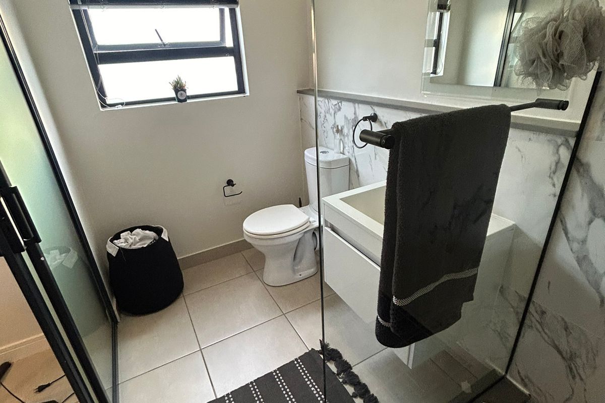 Modern bathroom featuring a vanity, toilet, and a glass-enclosed shower with marble-look wall tiling and neutral floor tiles.