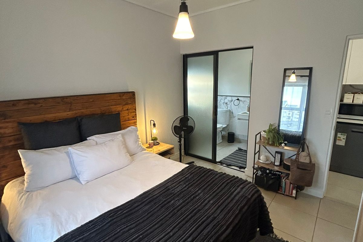 A well-maintained bedroom featuring tiled flooring, a modern pendant light, and direct access to an en-suite bathroom through a sliding glass door.