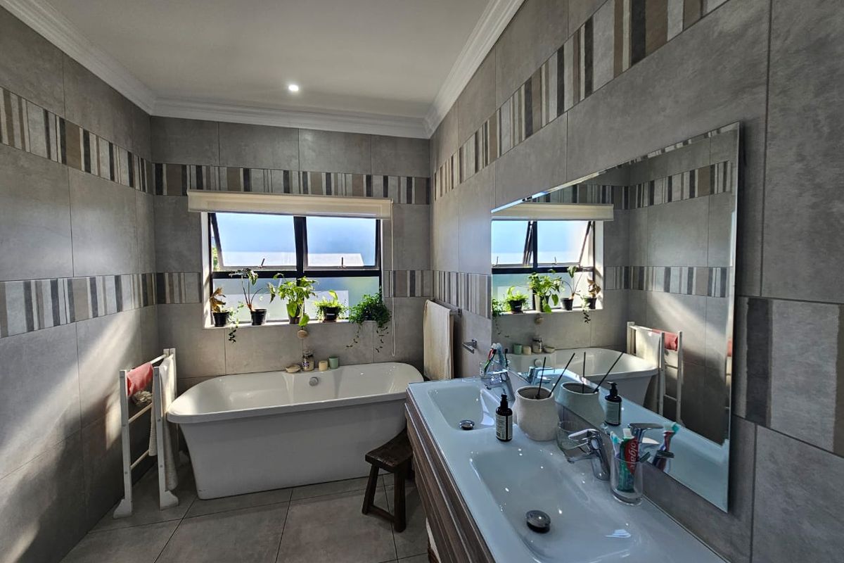 Modern bathroom featuring a freestanding bathtub, double vanity with large mirror, and contemporary grey wall tiling with decorative accent strips.