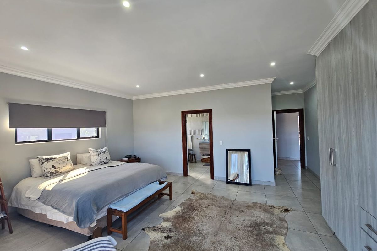 Spacious bedroom featuring neutral wall tones, tiled flooring, recessed downlighting, and ample built-in cupboard storage with an en-suite bathroom access.