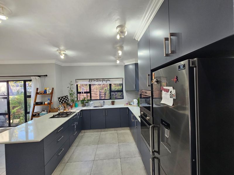 Modern kitchen featuring dark cabinetry, quartz countertops, built-in oven, gas hob, and tiled flooring with ample natural light.