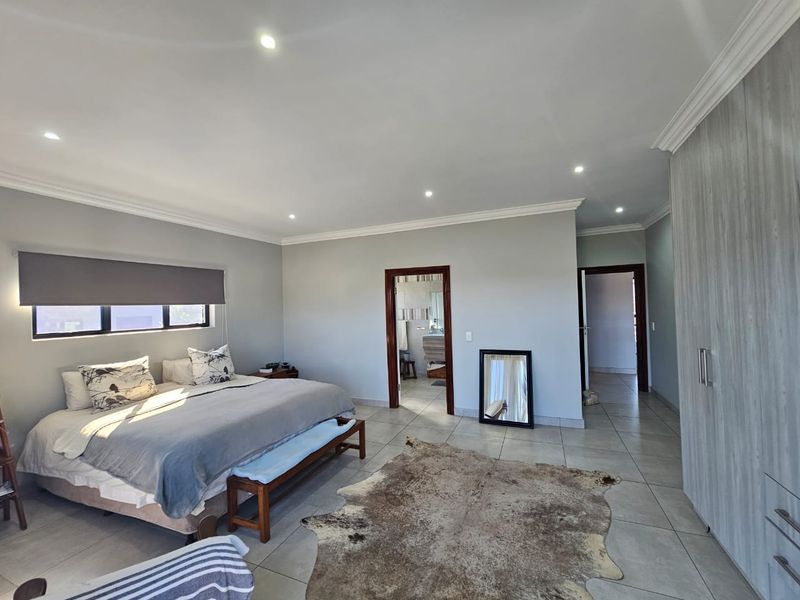 Spacious bedroom featuring neutral wall tones, tiled flooring, recessed downlighting, and ample built-in cupboard storage with an en-suite bathroom access.