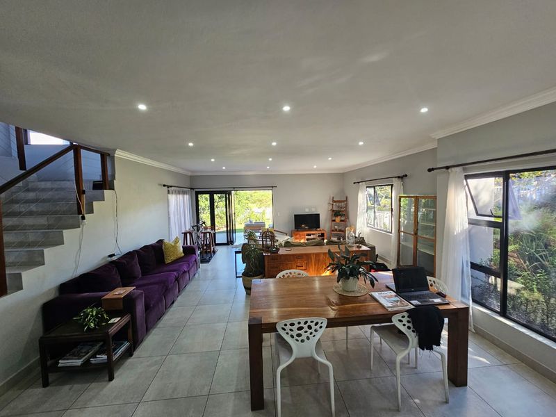 Spacious open-plan living and dining area featuring tiled floors, recessed lighting, and large windows providing ample natural light with direct access to the garden.
