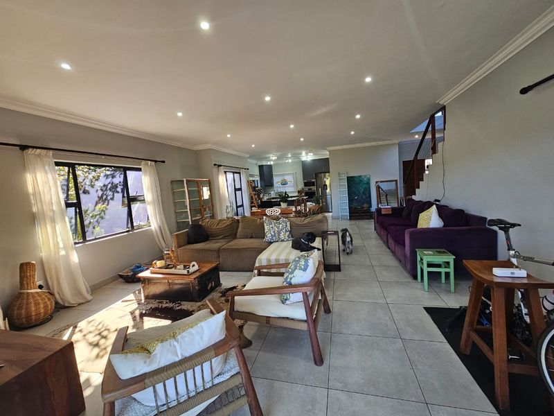 Spacious open-plan living area featuring tiled flooring, recessed downlighting, and a staircase, seamlessly connecting to the kitchen space.