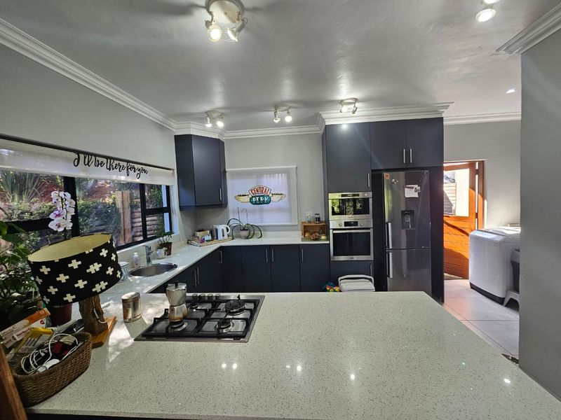Modern kitchen featuring dark cabinetry, quartz countertops, built-in oven, microwave, and gas hob, with direct access to an adjacent laundry area.