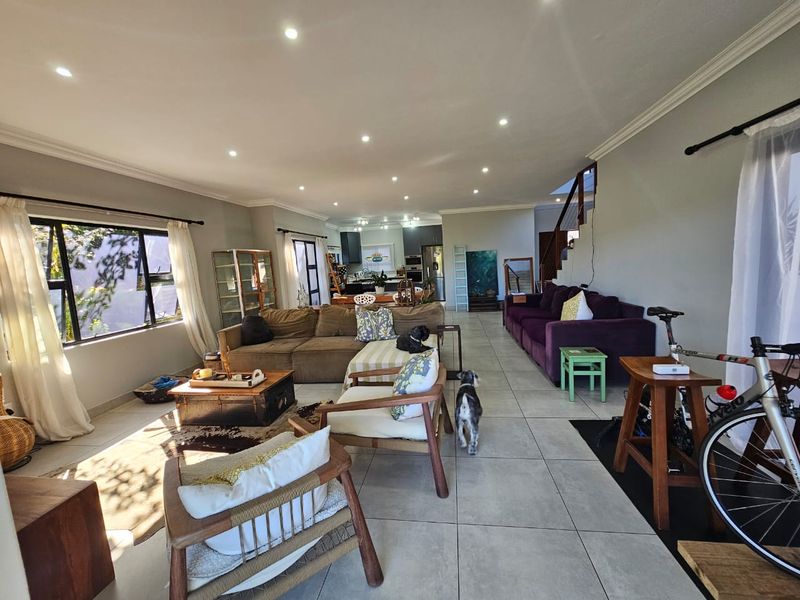 Spacious open-plan living area featuring large format floor tiles, recessed downlighting, and a seamless flow towards the kitchen and staircase.