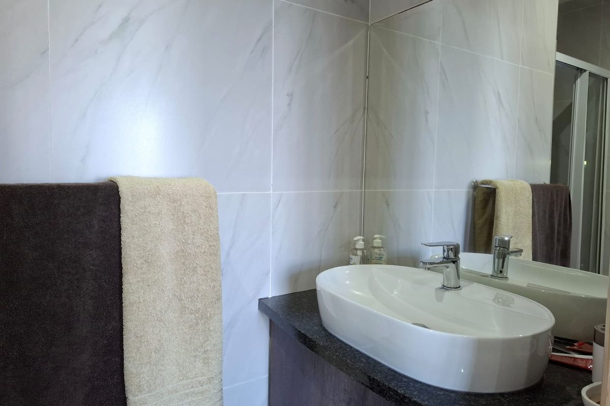 Modern bathroom featuring a vessel sink, chrome mixer tap, dark stone vanity countertop, and elegant marble-look wall tiles with a large mirror.
