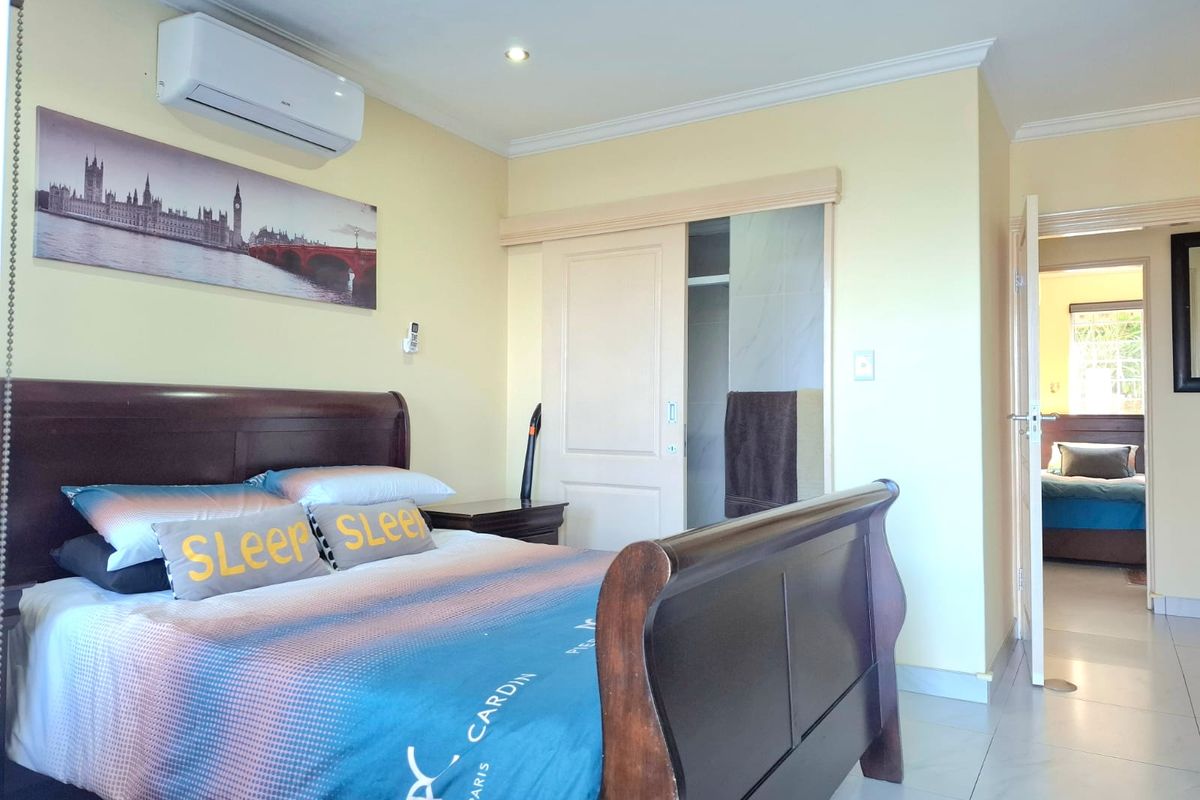 A well-maintained bedroom featuring tiled flooring, recessed lighting, and a wall-mounted split-system air conditioner, with an adjoining en-suite bathroom access.