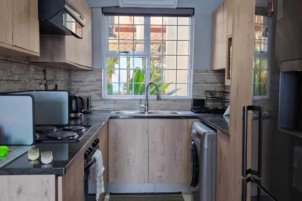 A well-maintained galley kitchen featuring modern wood-look cabinetry, stone-look countertops, integrated appliances, and a tiled backsplash with a window overlooking the exterior.