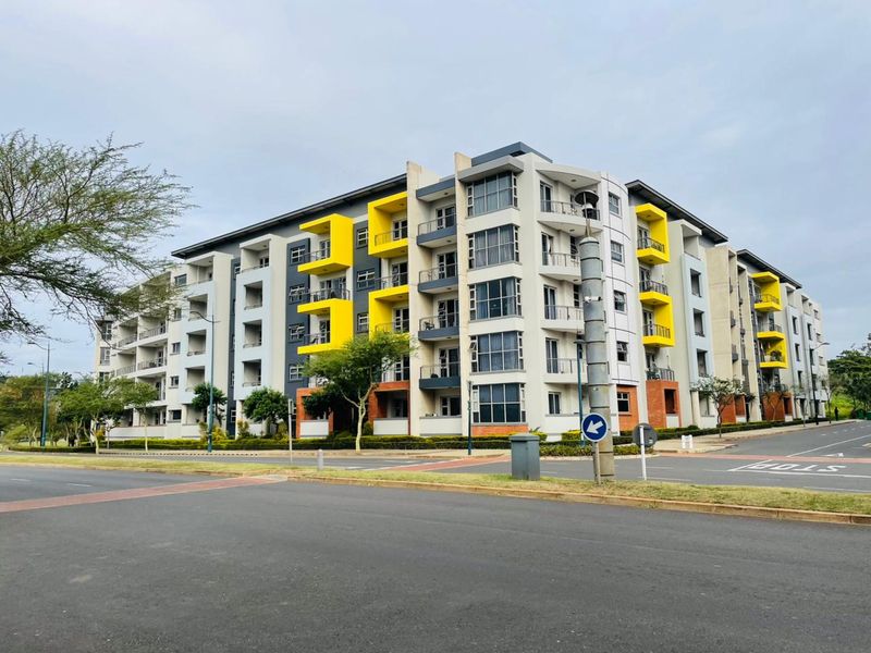 A modern multi-story apartment complex featuring a contemporary facade with yellow accent panels, private balconies, and well-maintained surrounding landscaping.