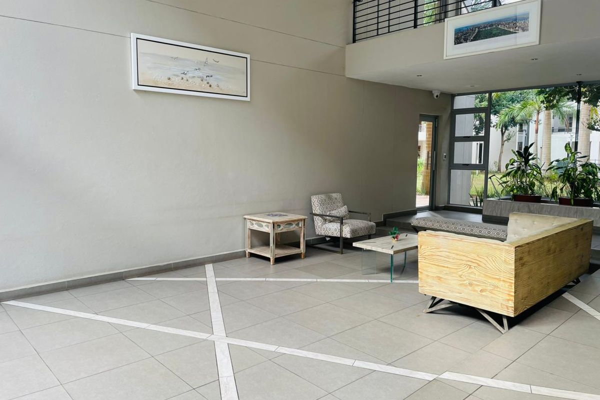 Spacious double-volume living area featuring large format floor tiles, a mezzanine level with metal balustrade, and abundant natural light through expansive windows.