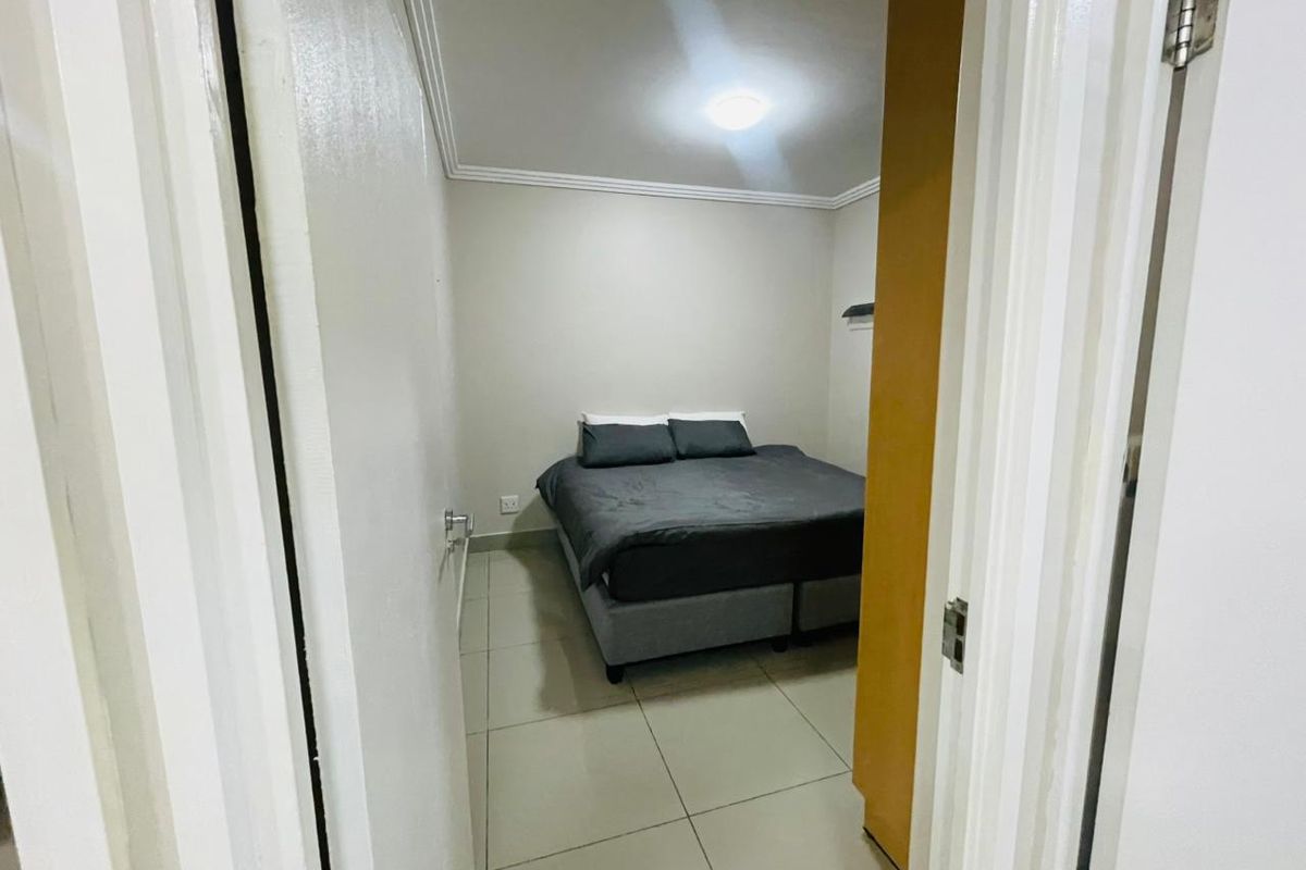 A compact bedroom featuring neutral wall tones, tiled flooring, and coved ceiling details, viewed from the doorway.