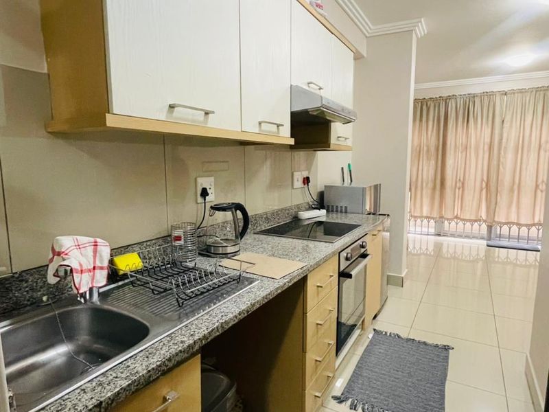 A functional kitchen featuring granite countertops, built-in cabinetry, an integrated oven, and a hob, with tiled flooring extending into the adjacent living area.