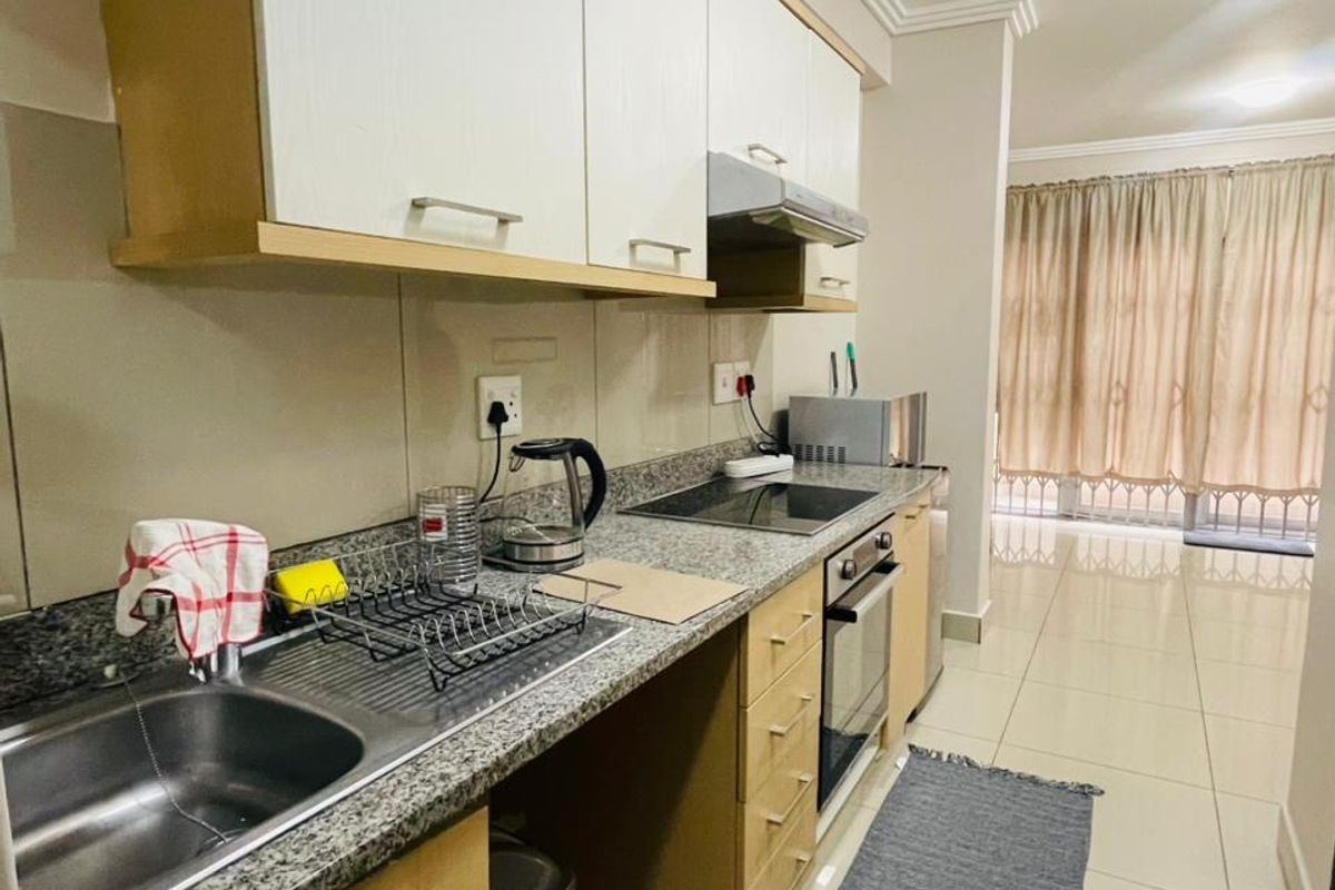 A functional kitchen featuring granite countertops, built-in cabinetry, an integrated oven, and a hob, with tiled flooring extending into the adjacent living area.