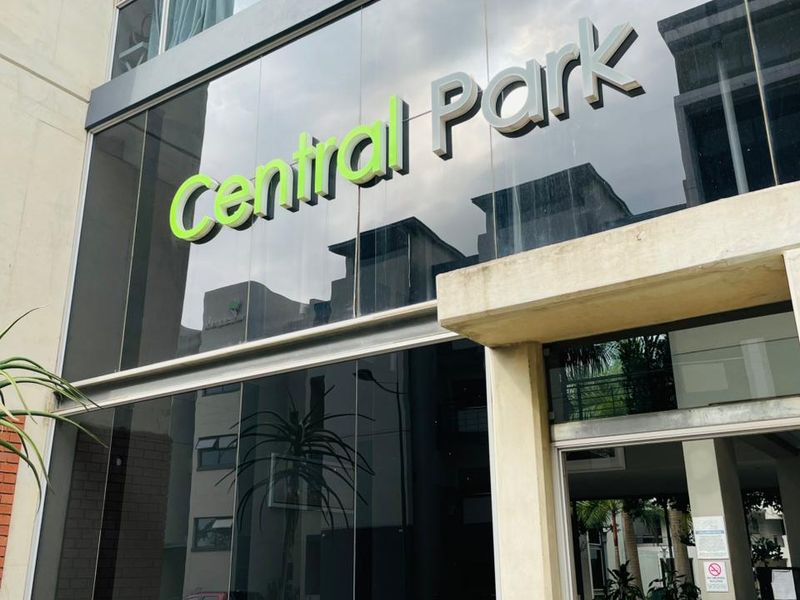 Modern apartment building entrance featuring a glass facade with prominent Central Park signage and a concrete canopy.