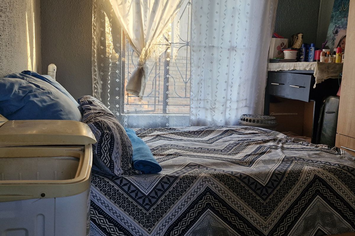A bedroom featuring a built-in wardrobe and a window with a security gate, providing natural light.
