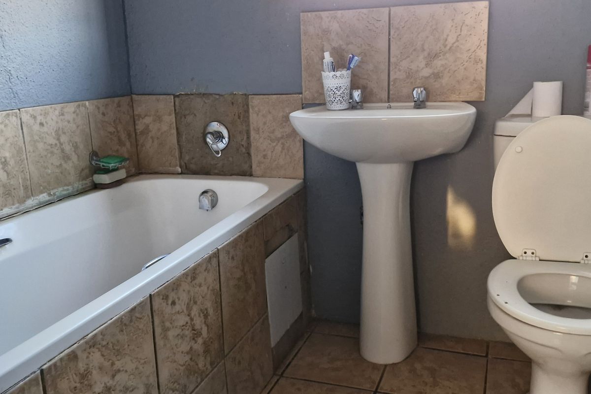 A functional bathroom featuring a pedestal basin, built-in bathtub, and toilet, finished with ceramic wall and floor tiles.