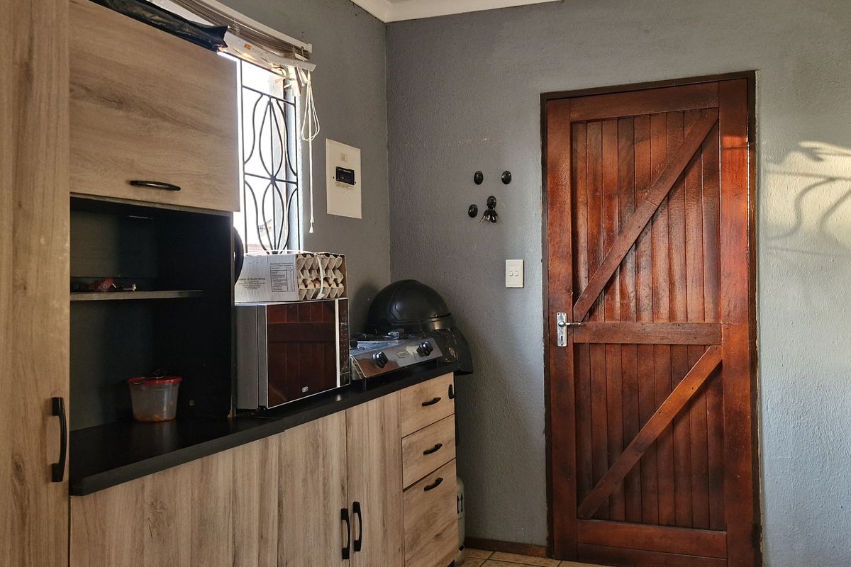 A functional kitchen area featuring wood-look cabinetry, dark countertops, and a solid timber door with a security gate.