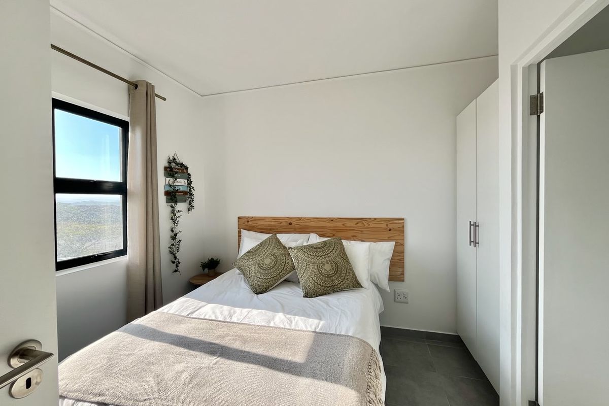 A bright and tidy bedroom featuring neutral tiled flooring, a built-in wardrobe, and a window with natural light.