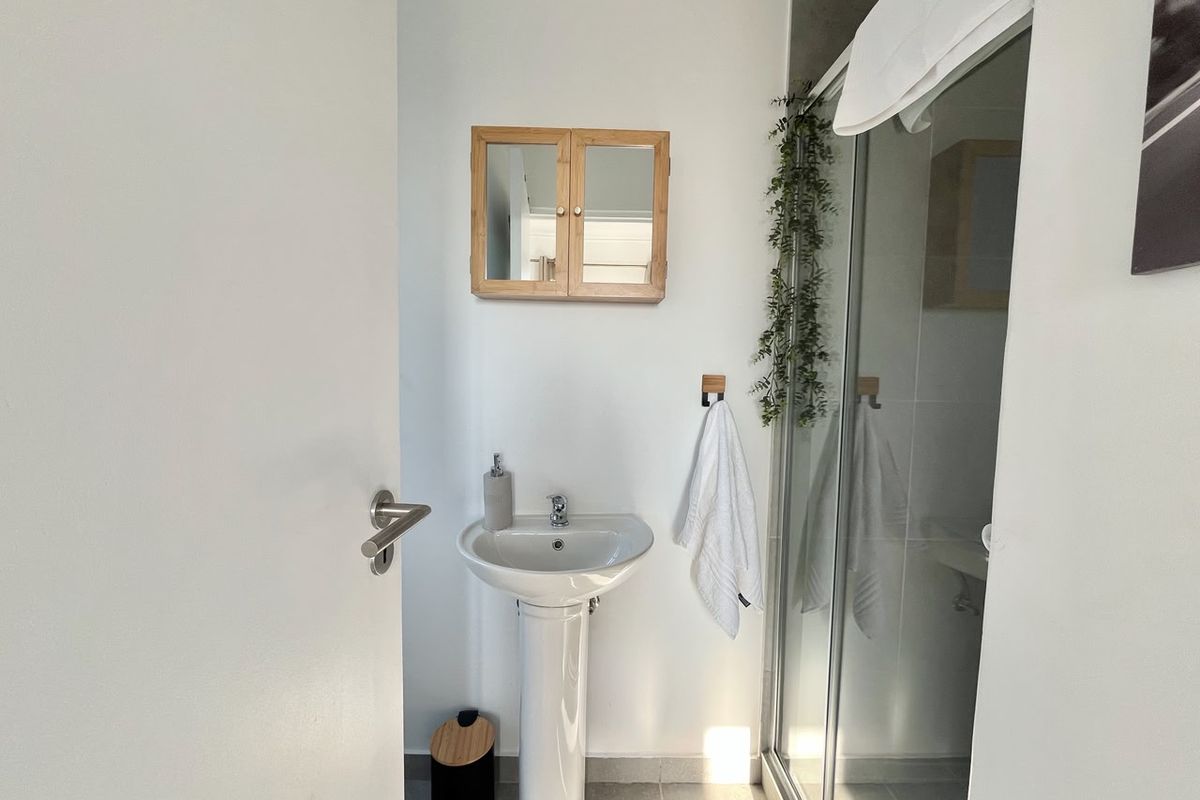 A clean and functional bathroom featuring a pedestal basin, a glass-enclosed shower, and a wall-mounted wooden medicine cabinet.