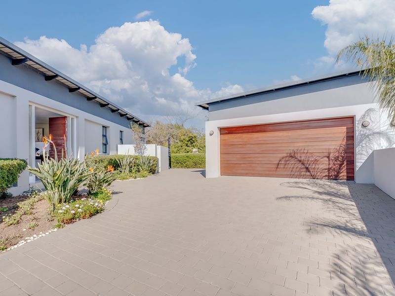 Modern front exterior featuring a paved driveway, timber garage door, and well-maintained landscaped garden beds under a clear blue sky.
