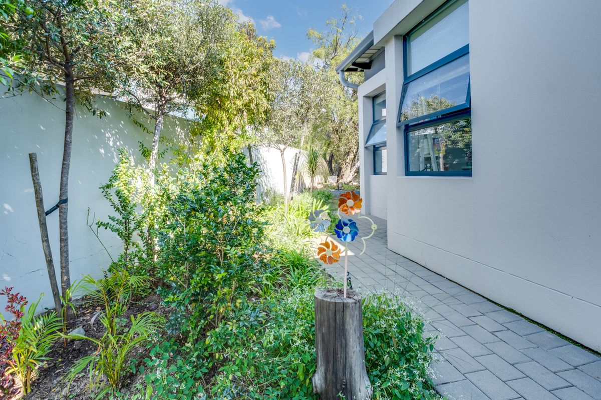 A side garden path featuring paved walkway, established greenery, and a boundary wall alongside the exterior of the house.
