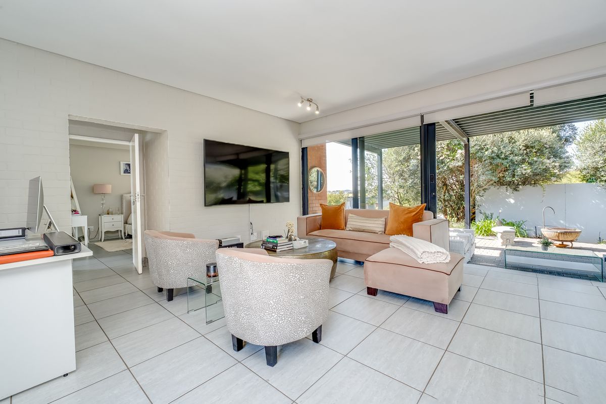 A bright and modern living room featuring large sliding glass doors that open onto a patio, with neutral tiled flooring and painted brick walls.