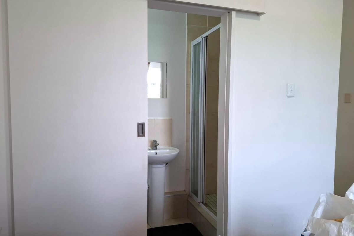 A compact bathroom featuring a pedestal basin and a separate shower enclosure, accessed via a space-saving sliding door.