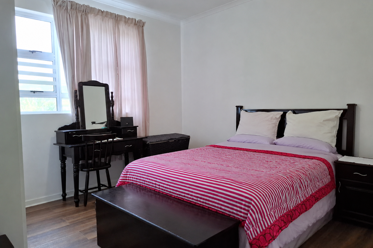 A bedroom featuring laminate flooring and a louvre window, providing a functional and neutral space for rest.