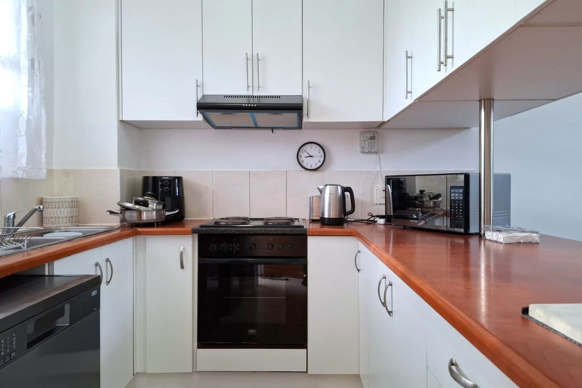 A functional kitchen featuring white cabinetry, wood-tone laminate countertops, a built-in oven with hob, and a tiled backsplash.